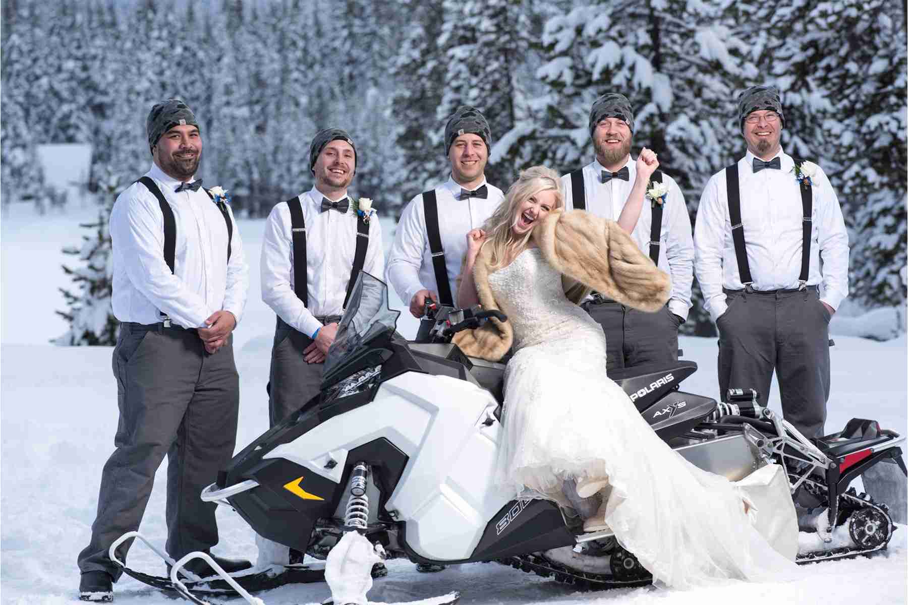 bride sitting on a snowmobile with her husband and his groomsmen at the back